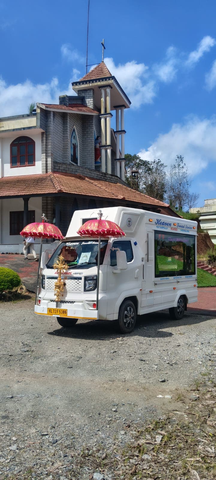 White hearse van with ceremonial umbrellas outside a hill parish church in Wayanad, Kerala