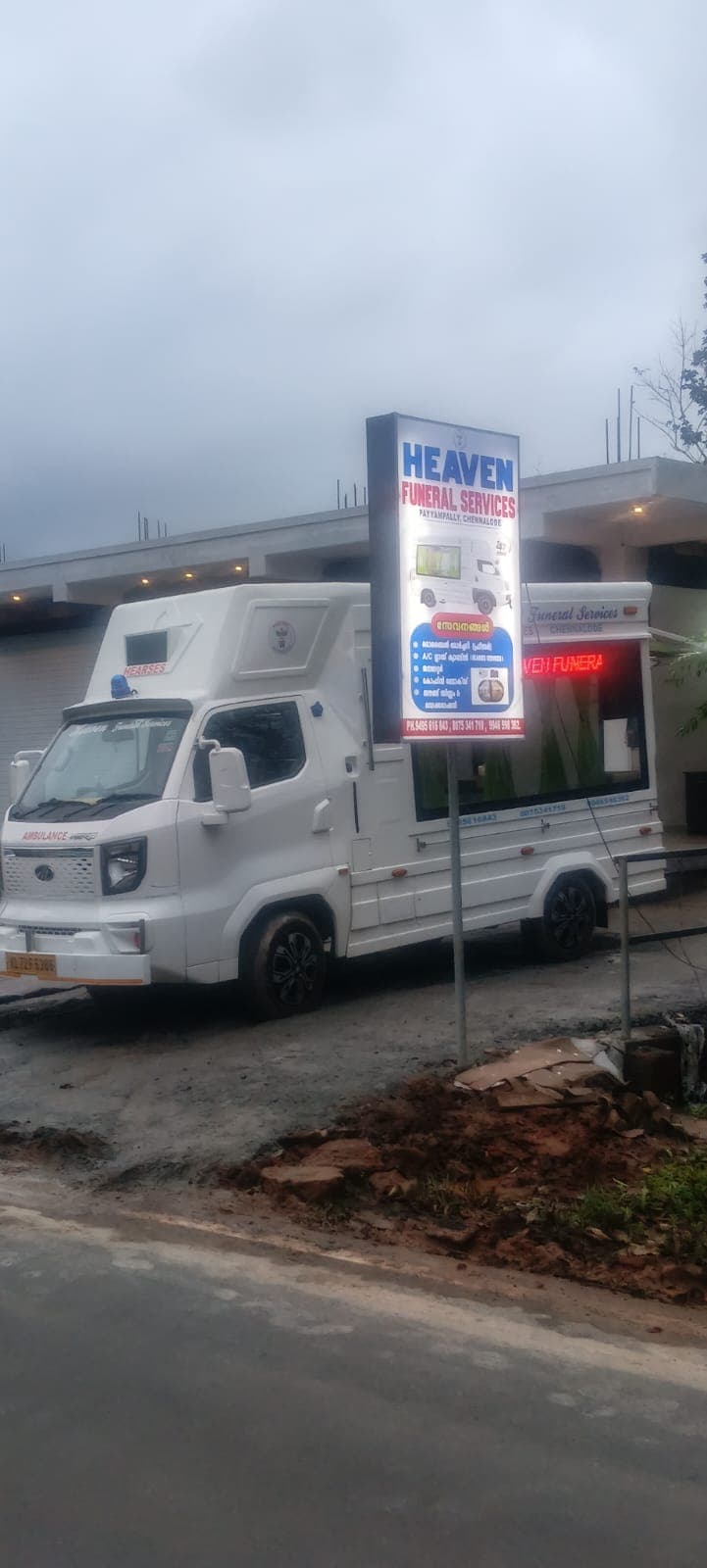 Heaven Funeral Services signboard lit at night beside the hearse van at the Chennalode shop in Wayanad