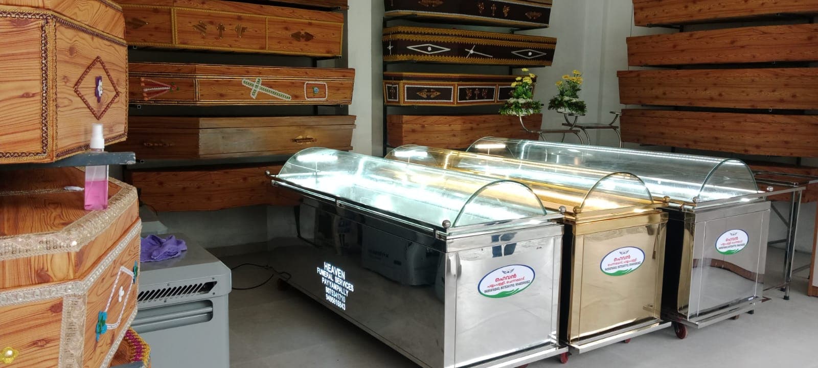 Mobile dead body freezer boxes with curved glass lids beside coffin racks at the Payyampally shop, Wayanad
