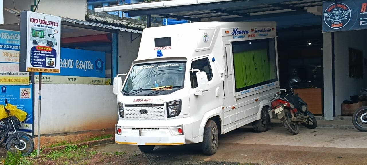Front view of the white Heaven Funeral Services hearse van beside the shop signboard