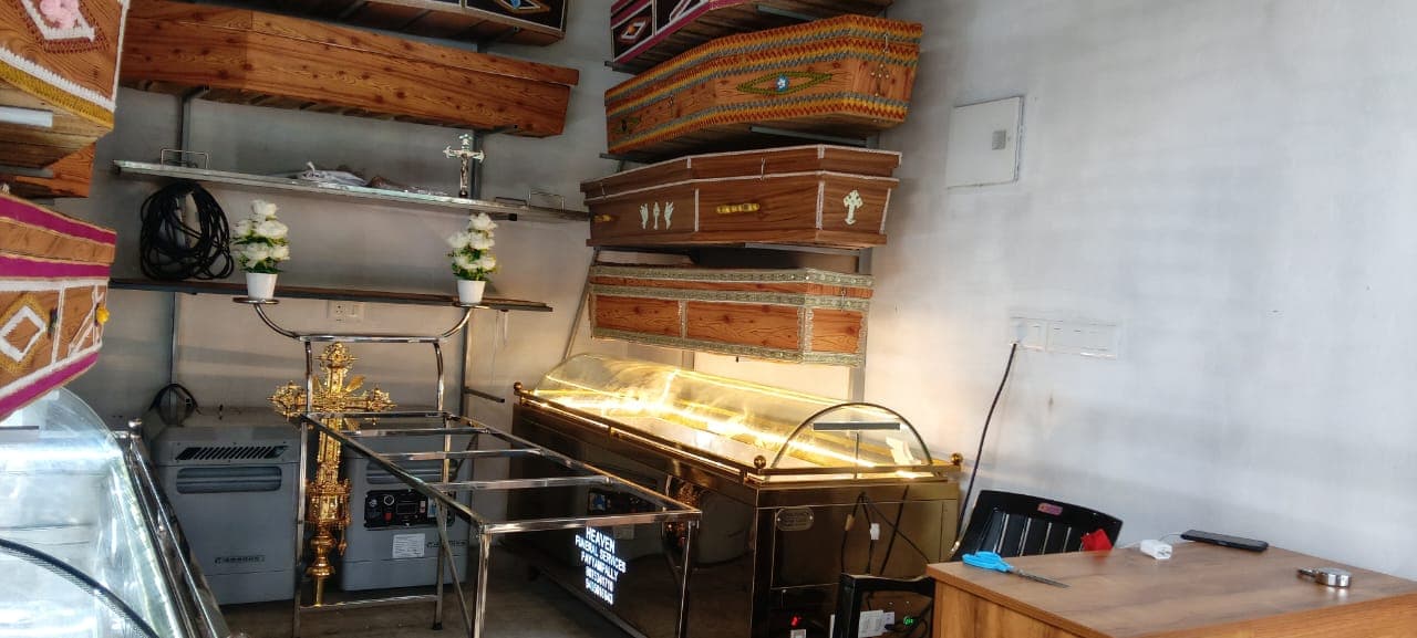 Heaven Funeral Services showroom display with coffins, a freezer unit, and floral arrangements
